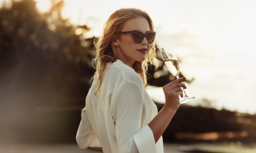 a woman sipping on wine outdoors in a bright dress
